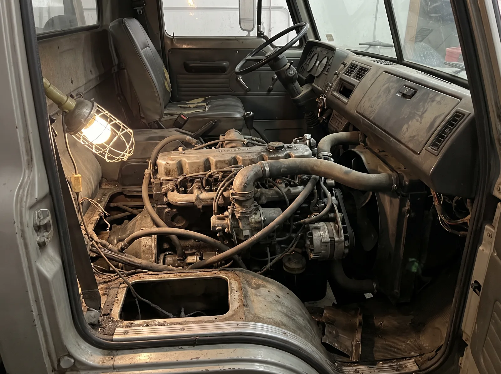 The engine of a cab over truck exposed under the lifted floor cover inside the cab