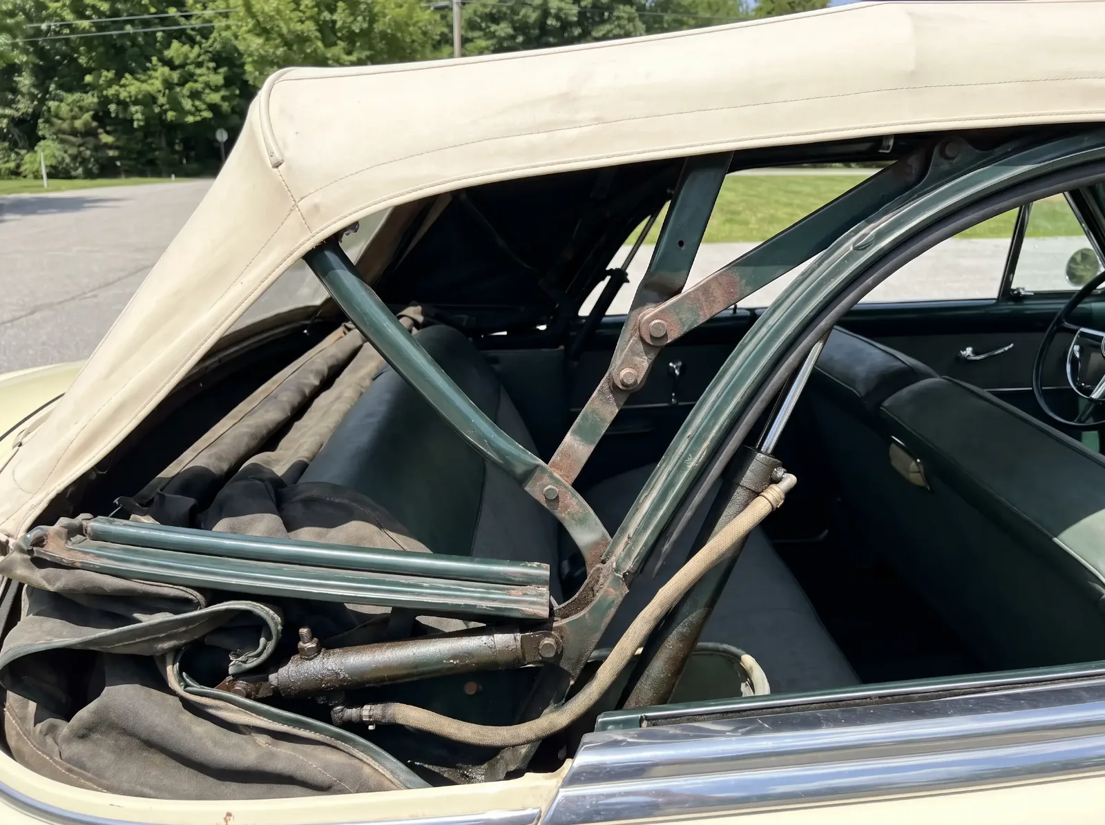 Convertible top mechanism halfway raised showing the steel bows, linkage and hydraulic ram cylinder
