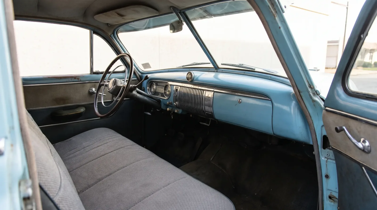 Interior of a 1951 Chevrolet showing the flat painted dashboard, thin steering wheel and cloth bench seat