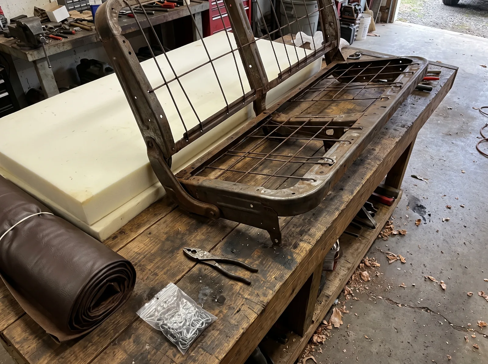 Bare bench seat frame on a bench with new foam, a vinyl cover and hog ring pliers