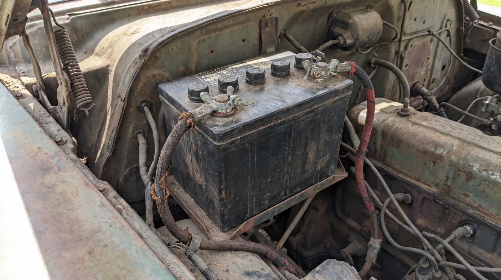 Battery in an early 1950s engine bay with the negative cable running to the engine block